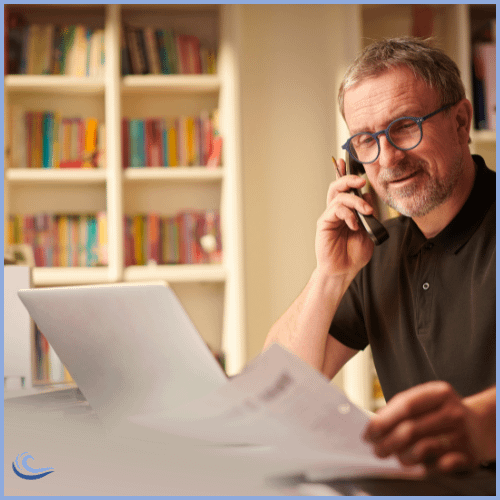 Man on the phone in front of a laptop with papers in his hand.